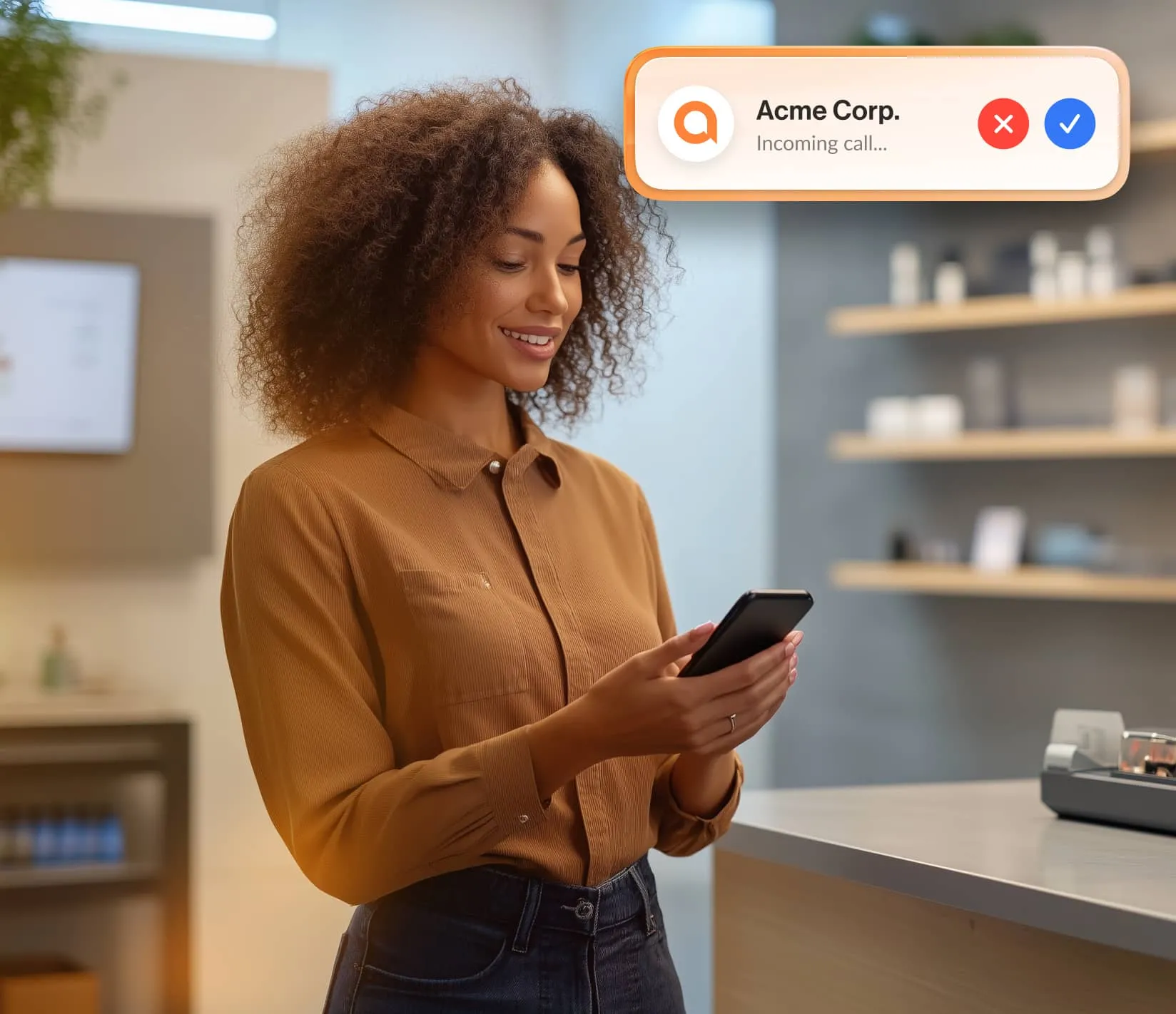 A smiling woman in an office glances at her phone, which displays an incoming call notification from the RingCentral app.