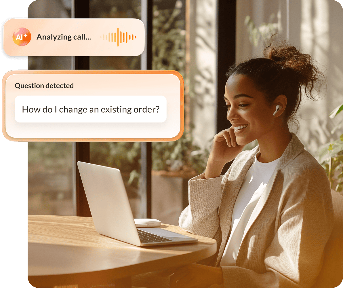 A smiling female contact center agent at home in front of a laptop with the RingCX AI assist feature on the foreground.