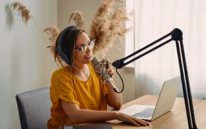 A woman on headphones hosting a virtual event at home using a big mic in front of her laptop